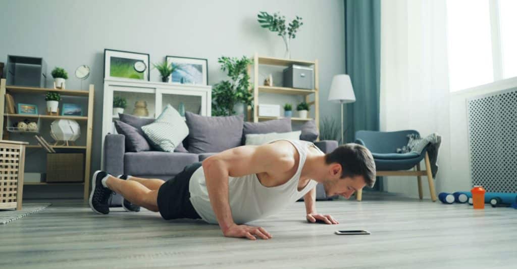 A man wearing a white tank top doing push-ups in a living room.