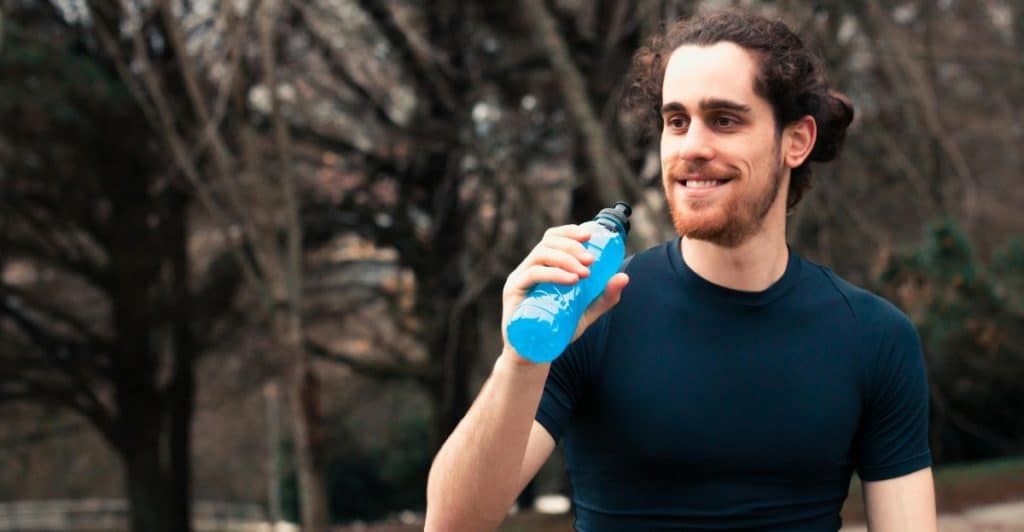 Smiling Man in Compression Shirt Holding a bottle of blue-colored energy drink