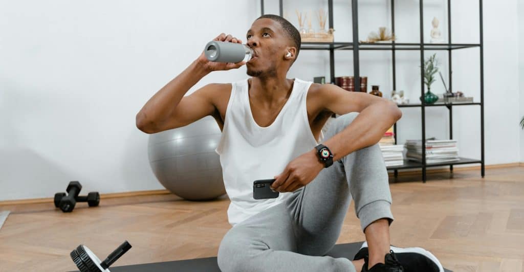 A man drinking from a water bottle indoors.