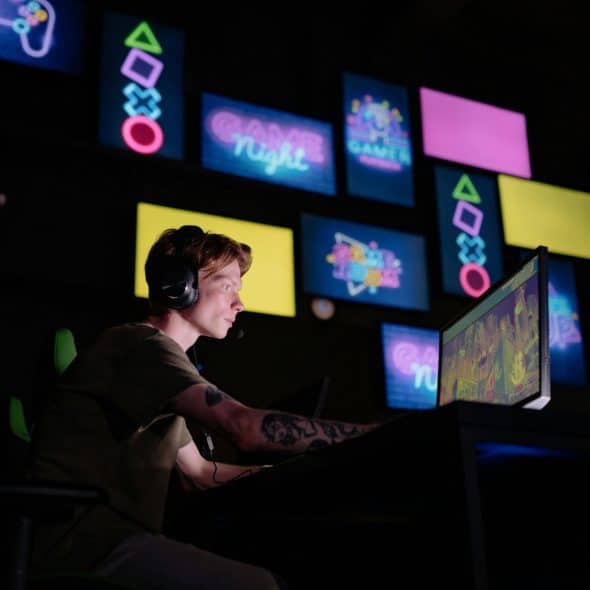 Tattooed man wearing headphones sitting in a gaming chair and playing video games.