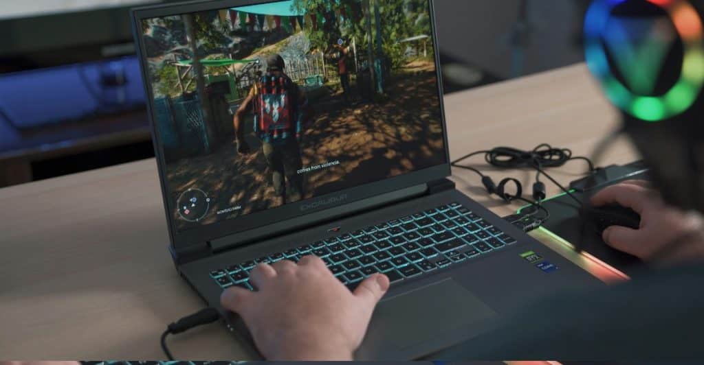 A person is sitting in front of a laptop, playing a video game with the screen showing a third-person perspective of a character in a colorful environment.