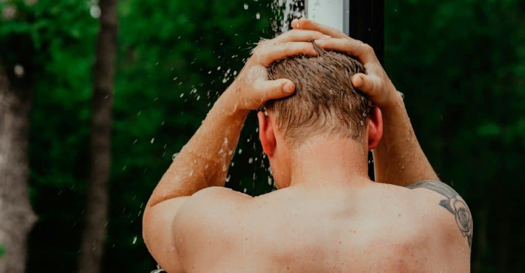 A person is rinsing their hair under an outdoor shower.
