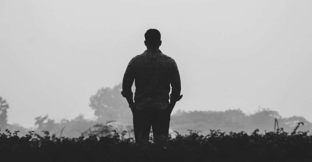 A silhouetted figure of a man standing alone in a misty outdoor setting.