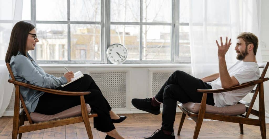 A man and woman sitting in chairs facing each other during a therapy session.