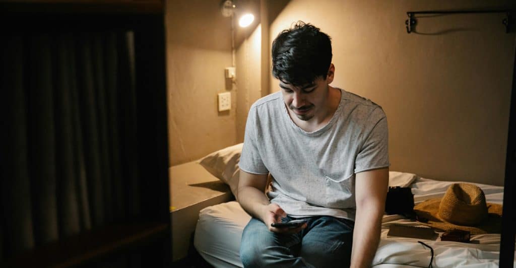 A person sitting on a bed looking at a smartphone.