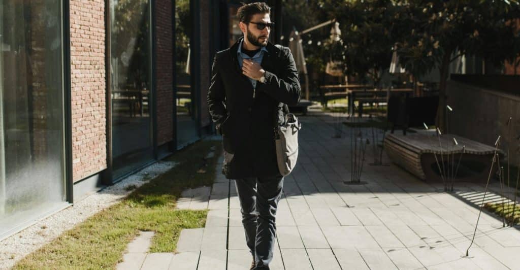 A man in a coat walking confidently along a city sidewalk.