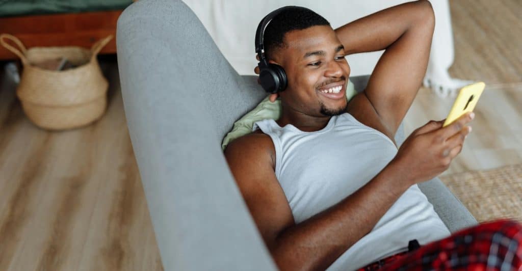 A man relaxing on a chair and looking at his phone while wearing Bose QuietComfort Ultra headphones.
