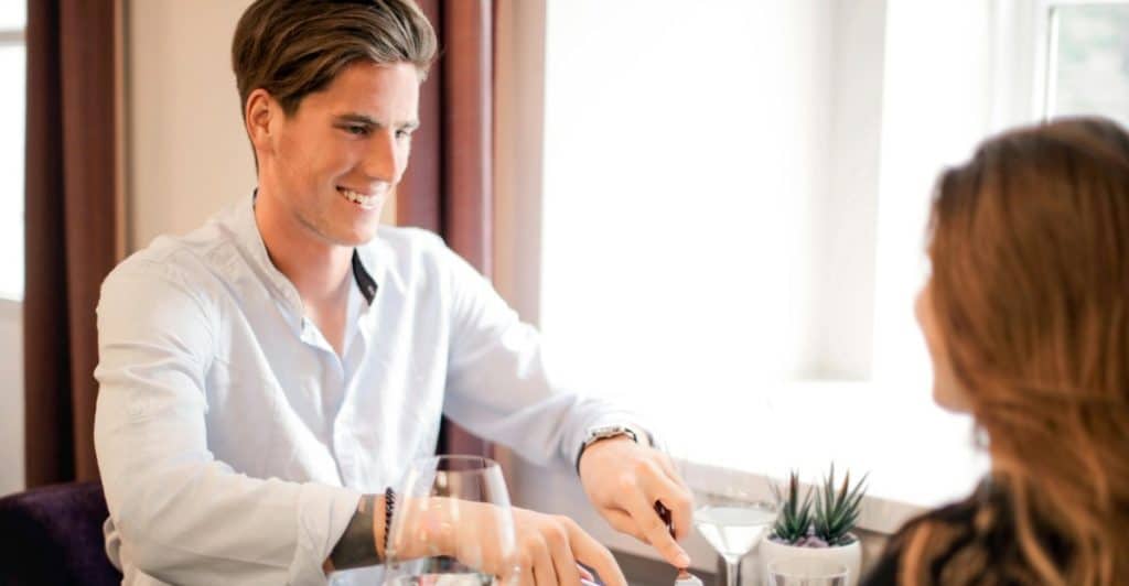 A man is seated at a dinner table, using utensils, while a woman sits across from him.