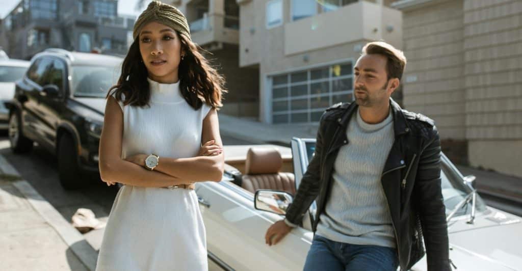 A man and a woman are standing outside, appearing to have a serious conversation.
