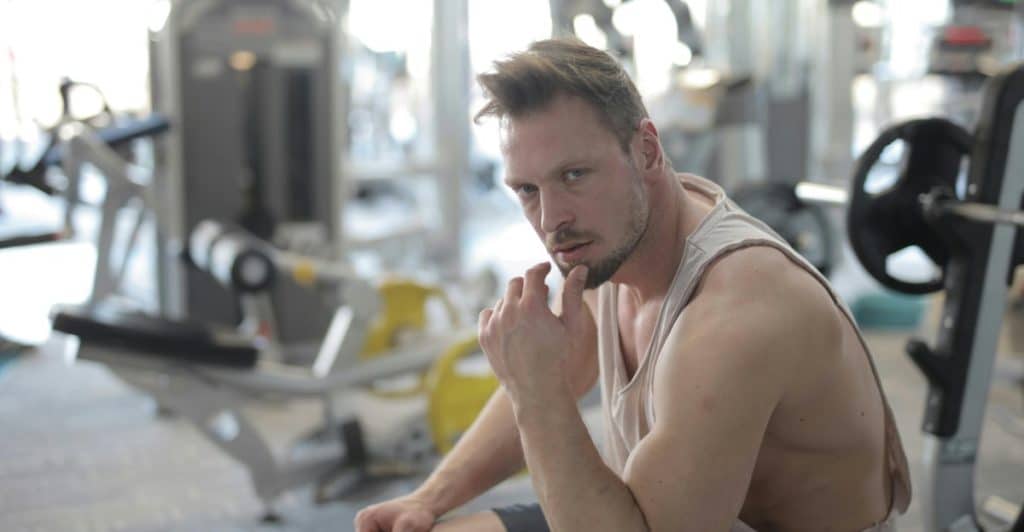 A man in workout clothes sitting and looking thoughtful in a gym.