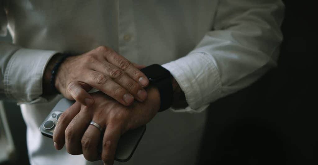  A person wearing a white shirt is looking at their watch and holding a phone.