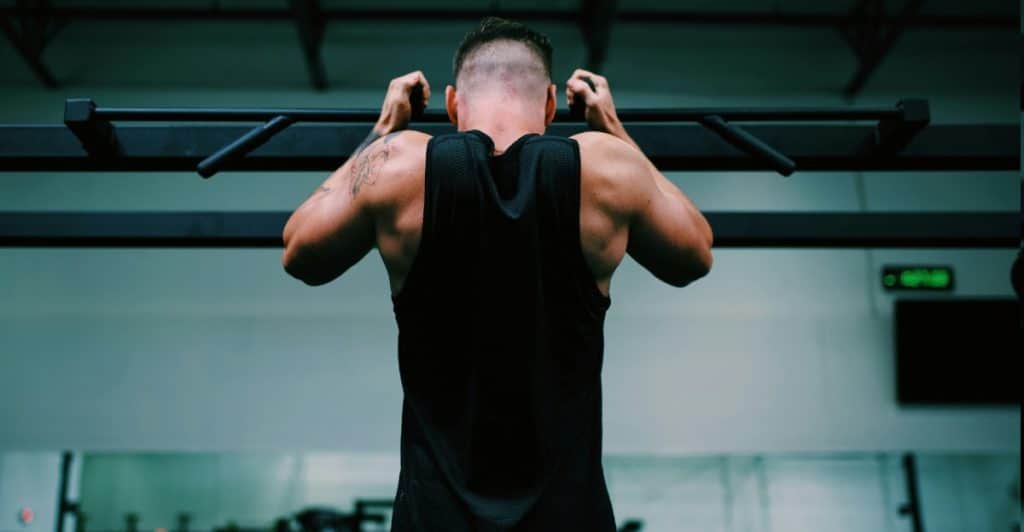 A muscular man is doing neutral grip pull-ups in a gym.