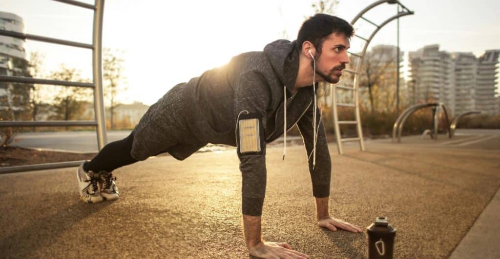 A man doing push-ups on an outdoor track with a water bottle nearby.