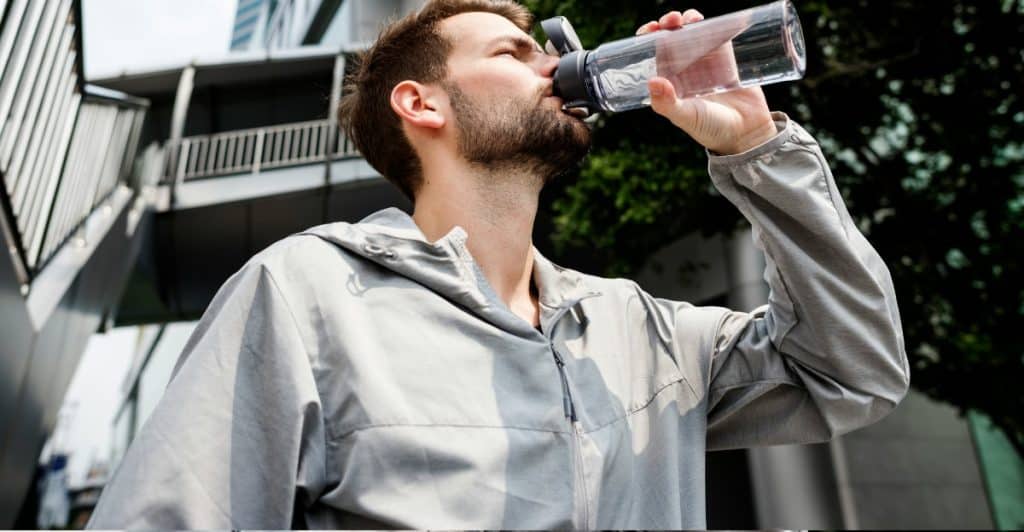 A man in athletic wear is drinking from a clear water bottle outside.