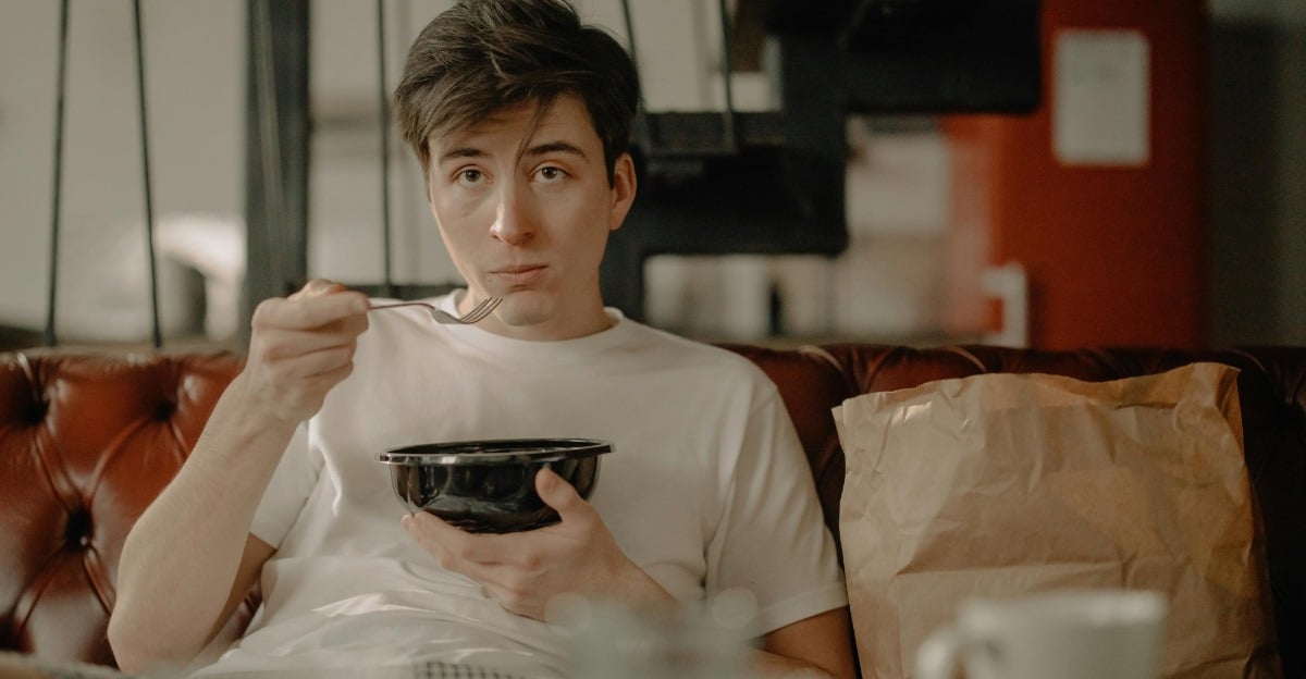 A man sitting on a couch eating from a black bowl.