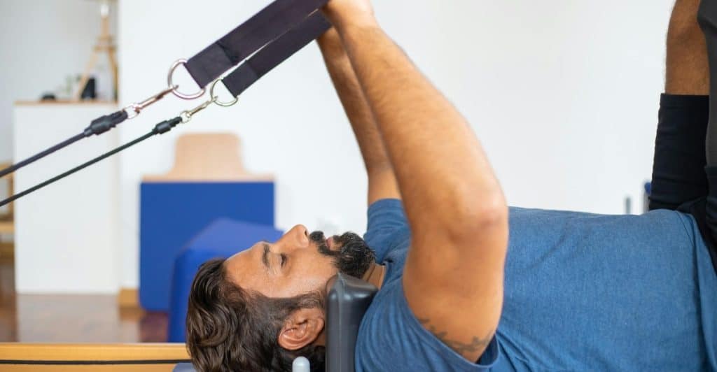A man using cables on an exercise machine while lying on a bench.