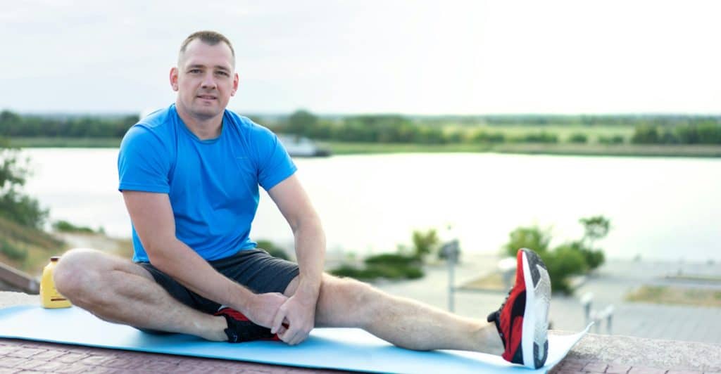 A man stretching on a yoga mat outdoors.