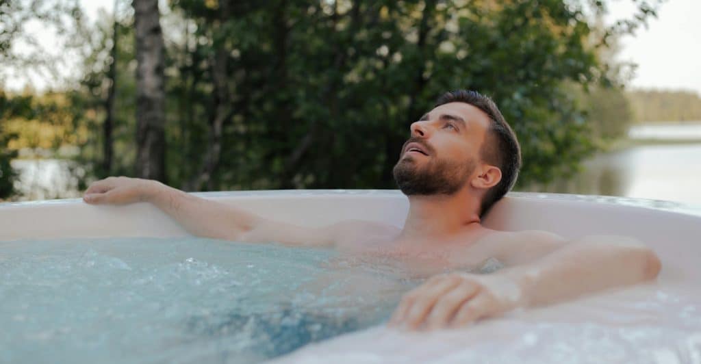 A person relaxing in a hot tub surrounded by nature.