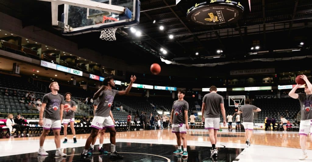 Several men playing basketball on a court in an arena, wearing matching gray t-shirts and white shorts.