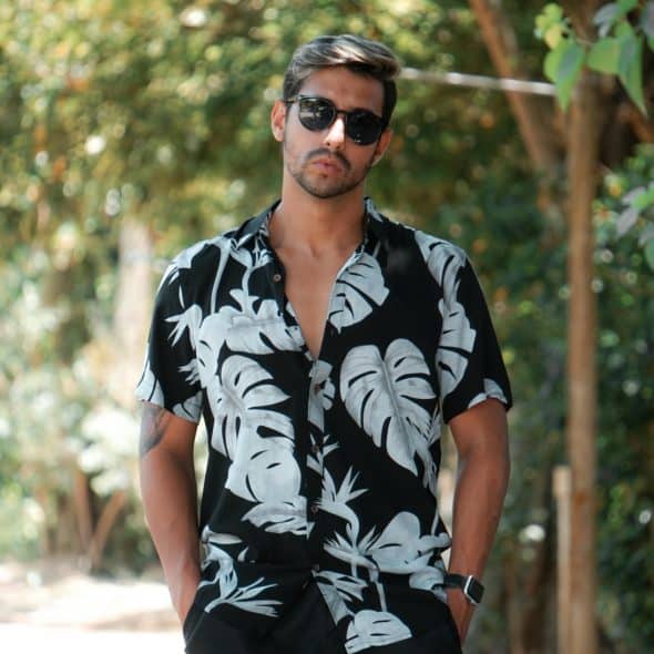 A man in a floral shirt and sunglasses standing outside.