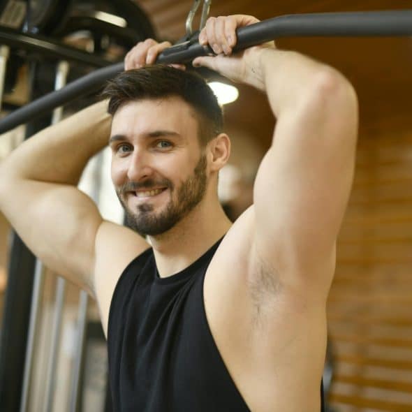 Smiling Man wearing a black tank top holding a lat pulldown machine handle.