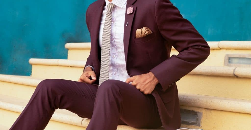 A man in a maroon suit sitting on stairs.