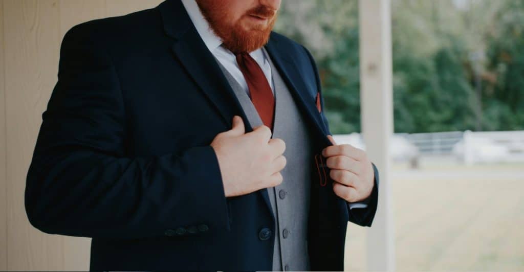  A man in a suit jacket and vest adjusting his jacket.
