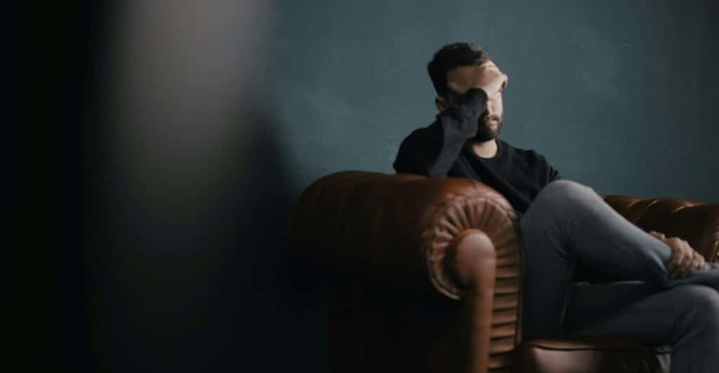 A man sitting in a chair, looking distressed and covering his face.