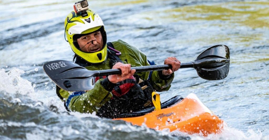 A man in a kayak with a paddle on a body of water.