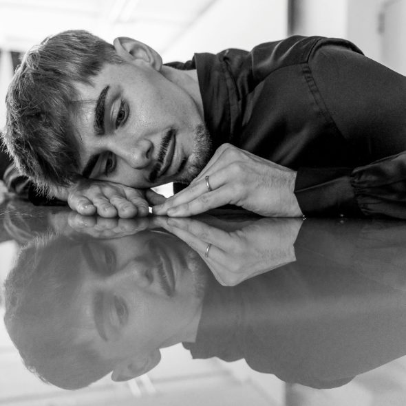 A man with short hair is lying on a reflective surface, with his reflection visible.