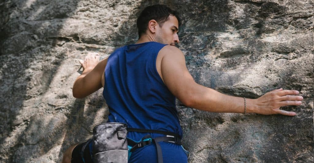 A man wearing blue tank top and shorts climbing a rocky cliff face.