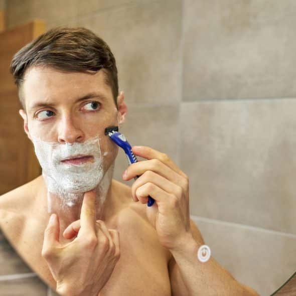 A man looking in a mirror and applying shaving cream to his face before shaving.