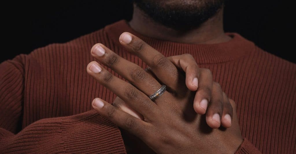 A man wearing a brown sweater is displaying his hands with a ring on one finger