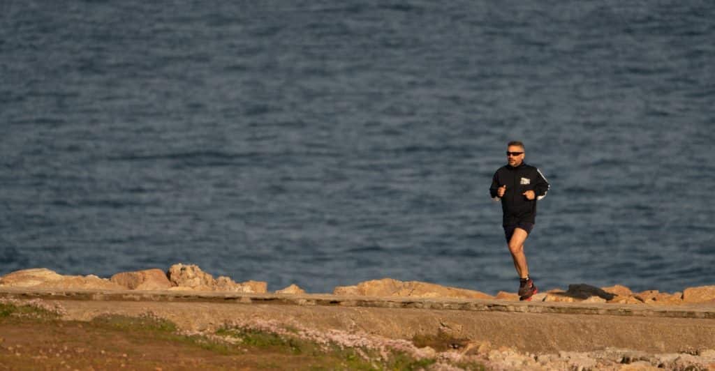 A man running along a rocky path by the sea.