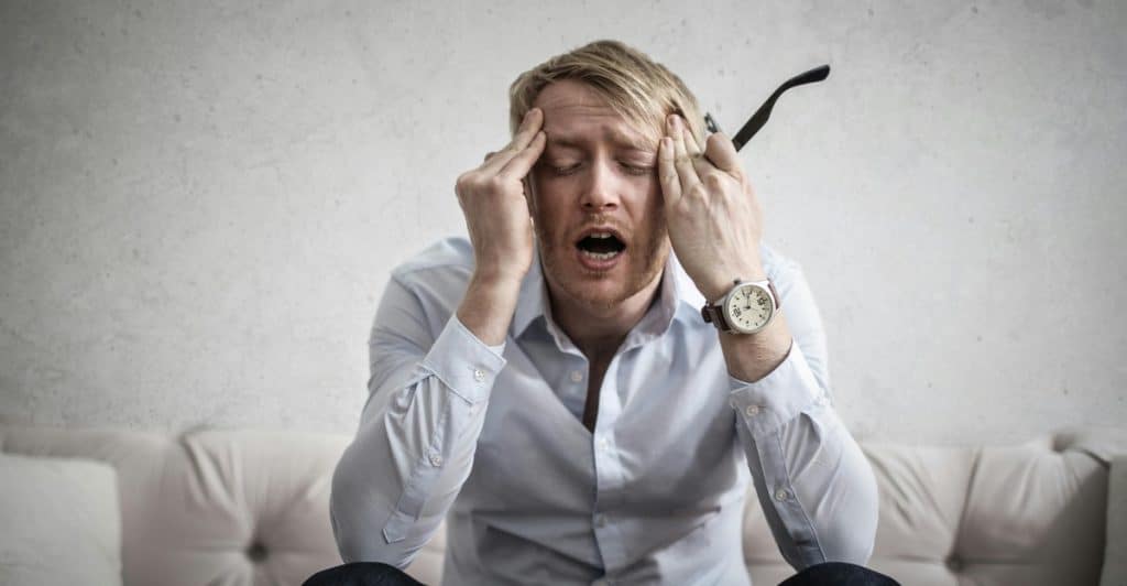 A man sitting on a couch with his hands on his head, looking stressed.