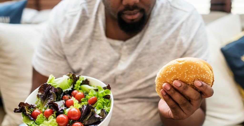 A man is holding a bowl of salad in one hand and a burger in the other.