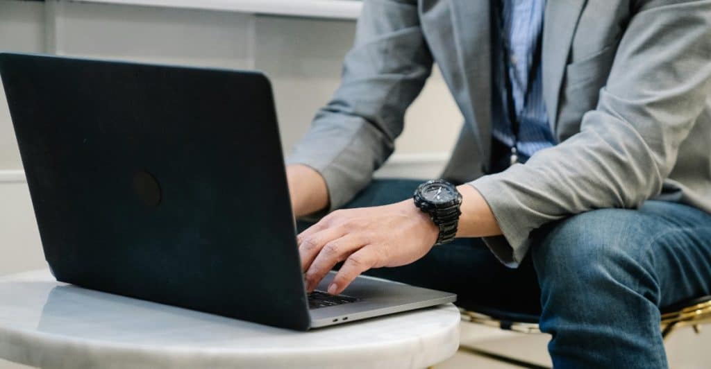 A man wearing a gray jacket is working on a laptop at a table.