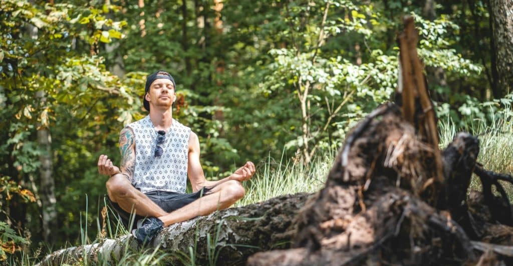 Man meditating on a fallen tree in the middle of a forest.