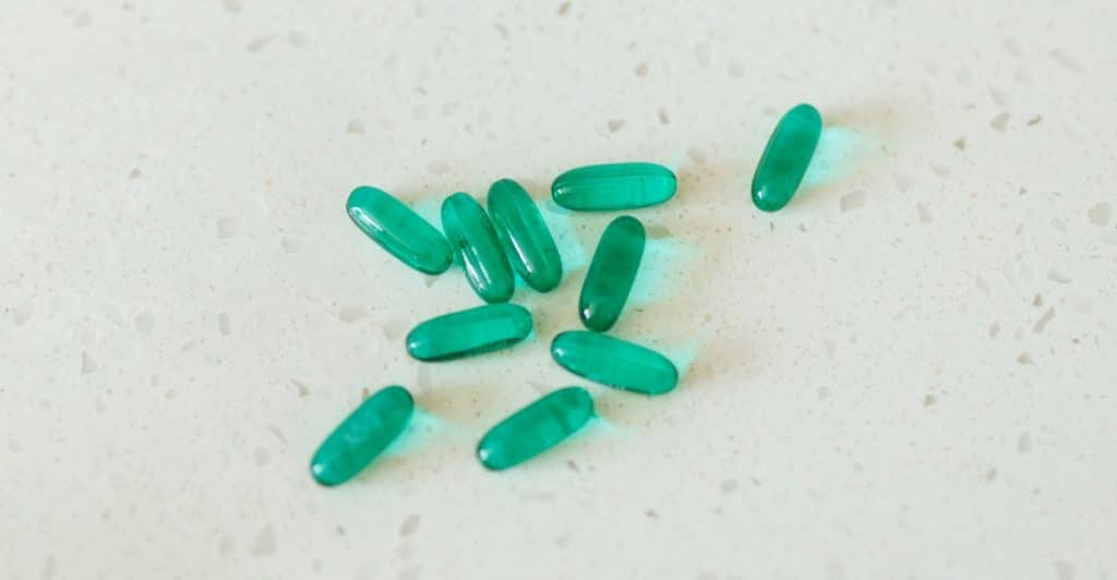 A small pile of green, oval-shaped melatonin capsules scattered on a white speckled surface.