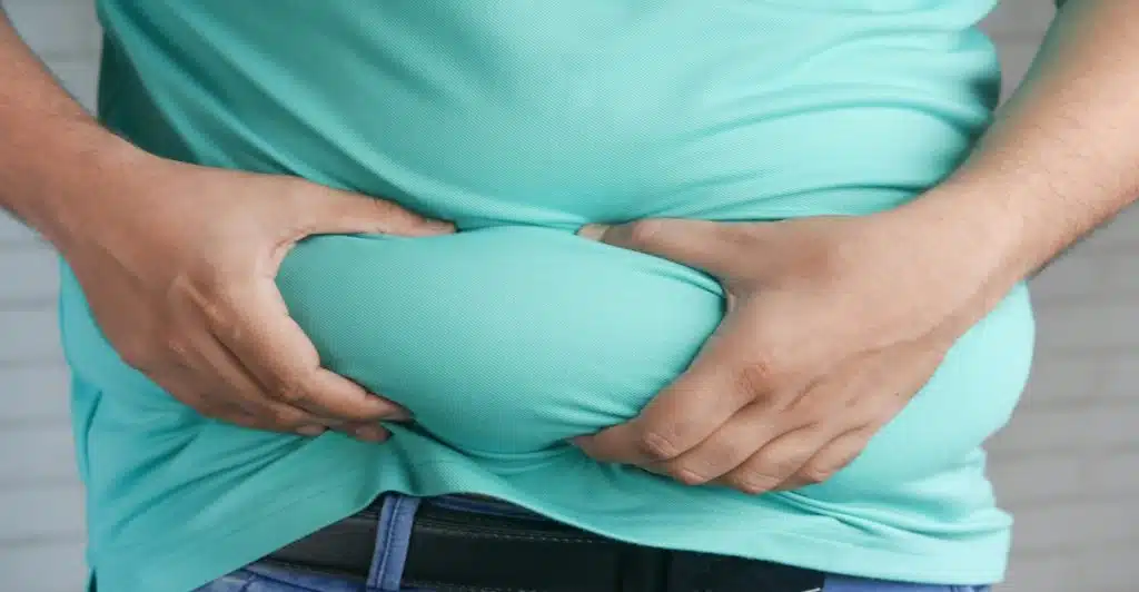 A close-up shot of a person's hands holding excess fat around their midsection.