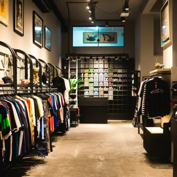 An interior shot of a clothing store with racks of colorful shirts on the left, a display of small items in the center, and clothing racks on the right.