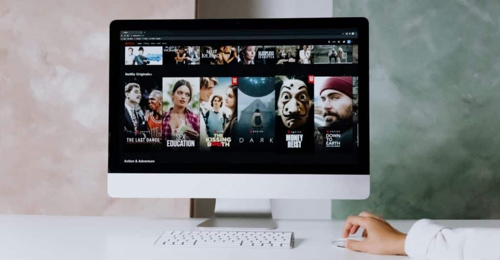 A computer monitor displays the interface of a streaming service with various movie and TV show titles and thumbnails.