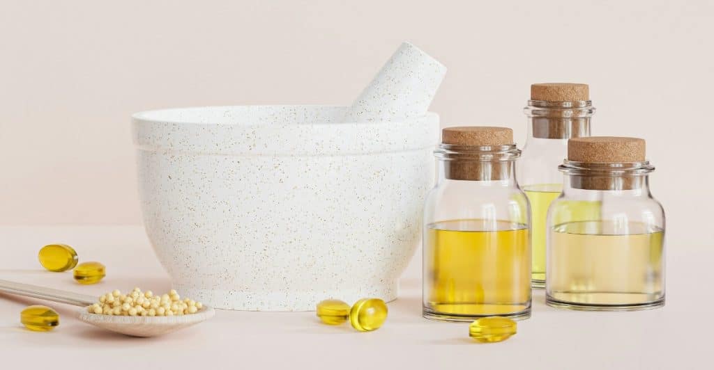 A still life arrangement of a mortar and pestle, yellow capsules, and small glass bottles of liquid.