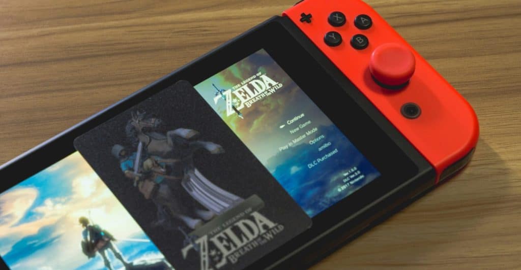 A close-up of a Nintendo Switch 2 console on a wooden surface, showing the screen with a game menu and the red and blue Joy-Con controllers.