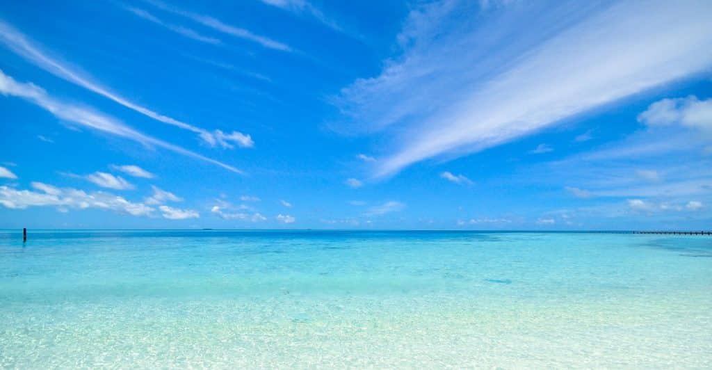 A bright, sunny scene of a clear blue ocean and white sand.