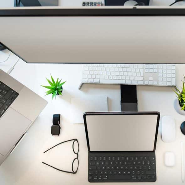 A birds-eye view of a desk setup with a laptop, monitor, keyboard, and other tech gadgets.
