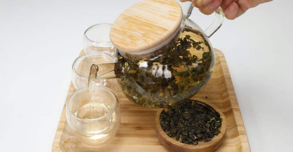 Person pouring oolong tea from a glass teapot into a glass cup.