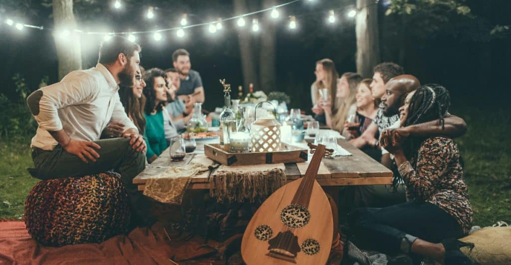 A group of people at an outdoor dinner party with string lights and a musical instrument.