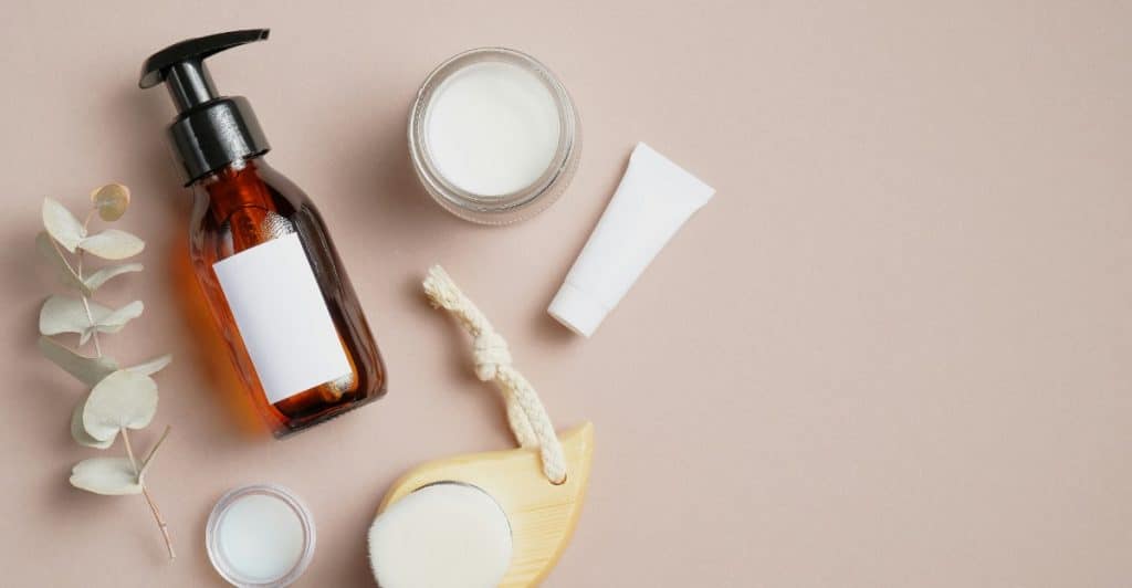 An overhead view of various skincare products and wooden bath accessories on a light surface.
