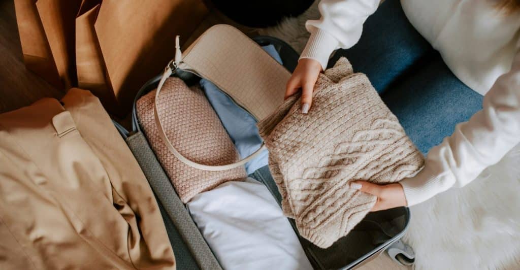 A person packing a suitcase with folded sweaters and clothes, preparing for travel
